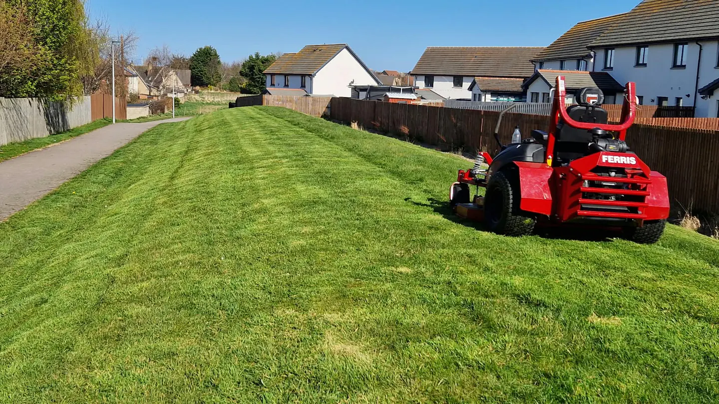 Ride-on mower maintaining shared grass beside homes on a housing estate